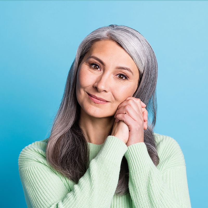 Smiling older woman with long gray hair and green sweater posing in the USA.