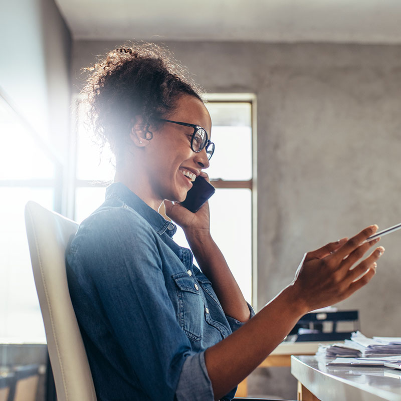A woman seated at a desk listing to on-hold messaging while on a call