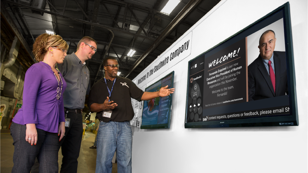 man showing two people examples of digital signage on a wall